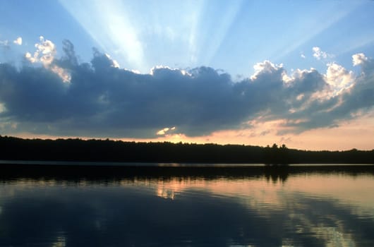 The setting sun creates a fan of rays from behind a cloud over Clark Lake in the Sylvania Wilderness Area.