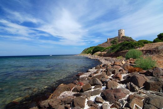 Really old lighthouse tower on the rock with sea on Sardinia