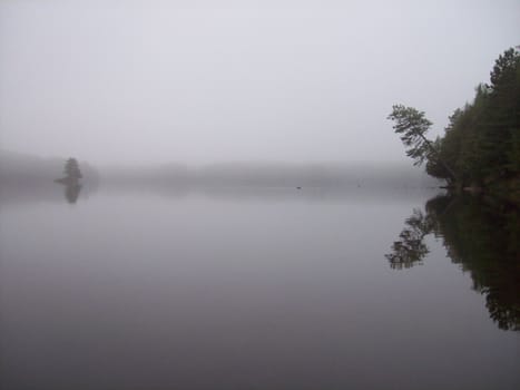 The fog and calm water make for a surrealistic scene.  The reflections of the shorelines and island add depth and interest to this photo.