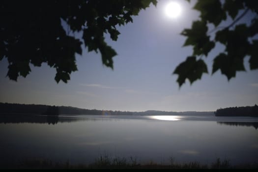 A full moon reflects on the placid water of a lake.  This time-exposure causes the scene to light up much like the daytime.