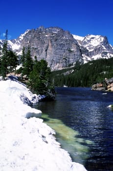 The blue, clear water of this mountain lake is contrasted by the bright snow in spring.  