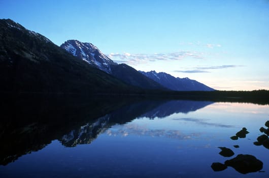 The Grand Teton mountain range is reflected in the early morning waters.  