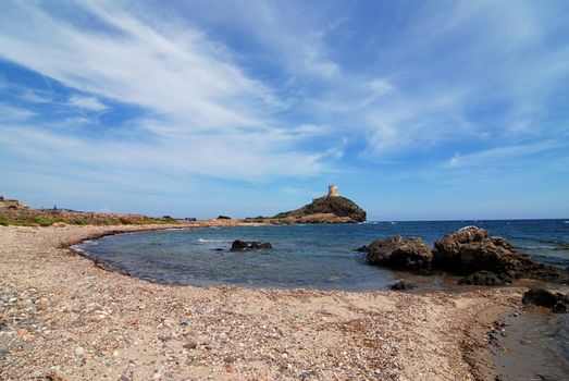 Beach and old lighthouse tower on the rock with sea on Sardinia