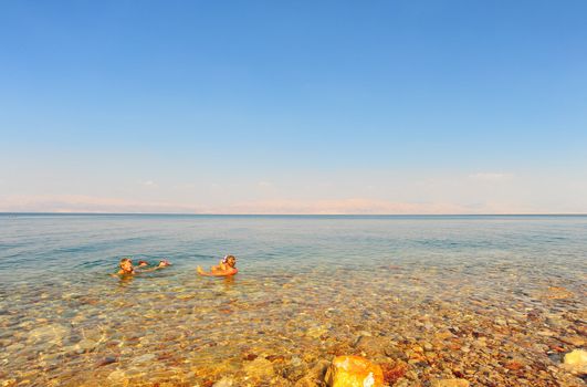 Woman And Boy Relaxing In Dead Sea Laying On Water Surface