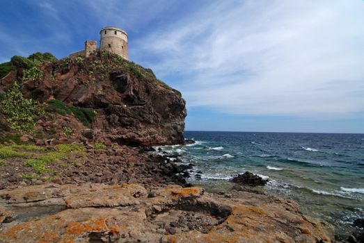 Ancient lighthouse on the rock with sea on Sardinia