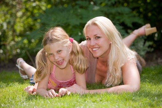 Blond mother with her daughter lying in the grass on a summer day