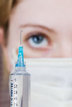 A syringe close-up with young nurse in background, focus on syringe.