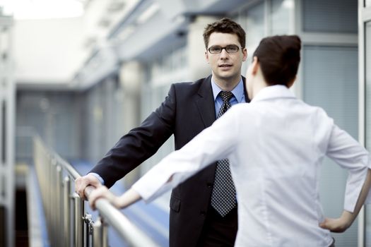 Business portrait - young man and woman standing and talking on modern office corridor