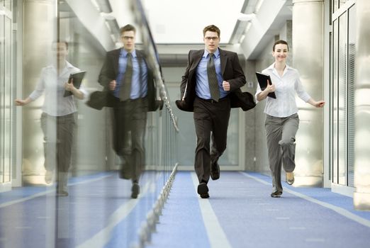 Businessman and businesswoman running on modern office corridor.