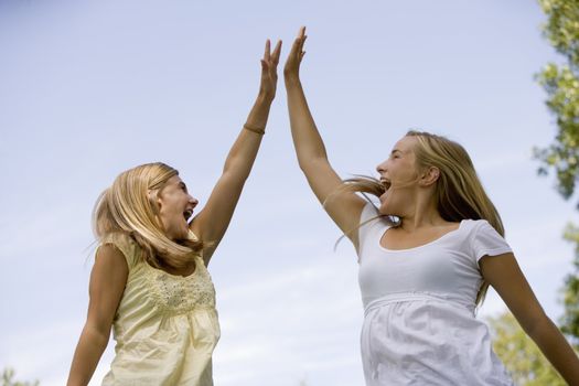 Teen girls celebrate winning by jumping in air and doing a high-five