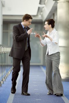 Businessman and businesswoman walking and talking on modern office building corridor.