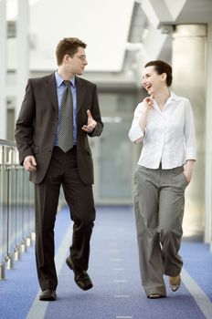 Businessman and businesswoman walking and talking on modern office corridor.