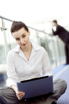Portrait of young woman sitting with notebook on her lap in modern business office building corridor