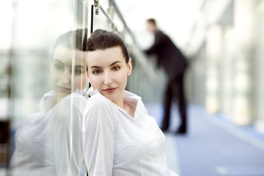 Portrait of young woman sitting on the floor in modern office building corridor and leaning against glass balustrade