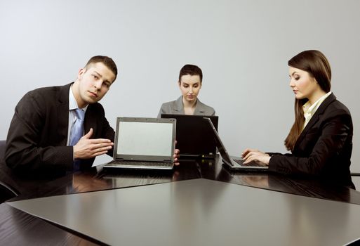 Business group portrait - Young man presenting something on the screen of his computer and two women working on their laptops