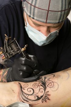 A tattoo artist applying his craft onto the leg of a female. Property release supplied includes tattooists' artwork.