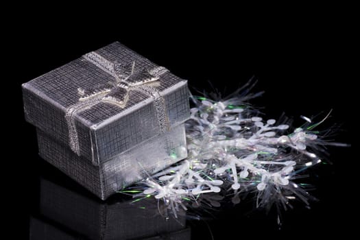Silver gift box and artificial snowflake on black mirror background