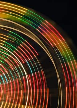 The colorful contours of a moving ferris wheel at night.