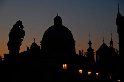 Outlines of buildings, spires, and statues in Prague at dawn.