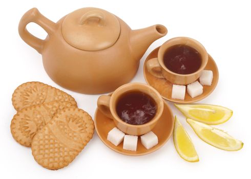 set of the earthenware teapot, two cups of tea, lump shugar, sliced lemon and biscuits isolated on white background with clipping path                      