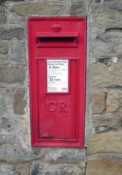 Red British post box on wall in rural setting.