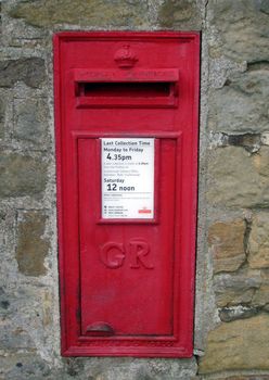 Red British post box on wall in rural setting.