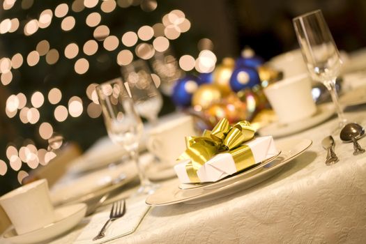 Gold present on dining table with Christmas tree lights in background