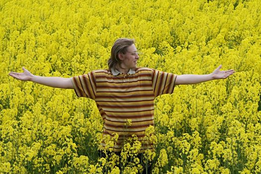 Happy and smiling young man in the yellow flower meadow.