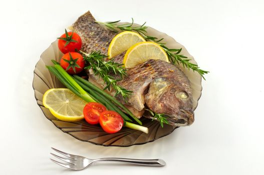 
Fried carp on a plate with tomatoes, lemon, onion and rosemary