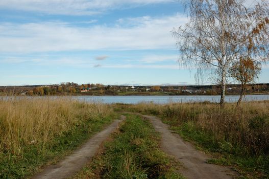 Ground country road to a flat riverbank, autumn