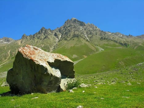 The fragment of a rock lays on a green meadow on a background of mountain
