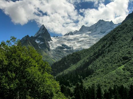 The mountain covered with a snow on a background of the blue sky with white clouds