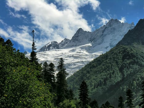 The mountain covered with a snow on a background of the blue sky with white clouds