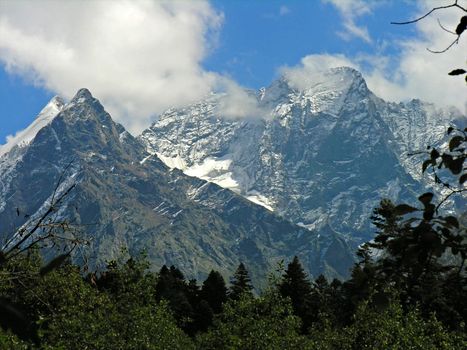 The mountain covered with a snow on a background of the blue sky with white clouds