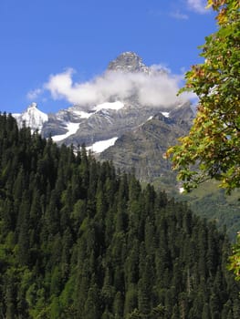 The mountain covered with a snow on a background of the blue sky with white clouds