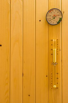 Hourglass, thermometer and hydrometer on wooden wall in sauna.