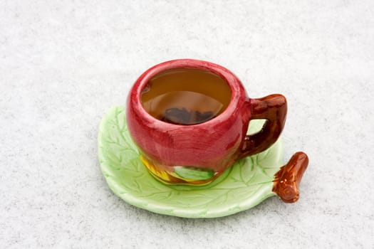 In the center of the frame cup of black tea on a snowy background. Saucer shaped leaf. 