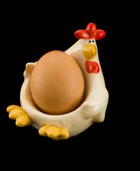 Chicken holding egg, isolated on black background.