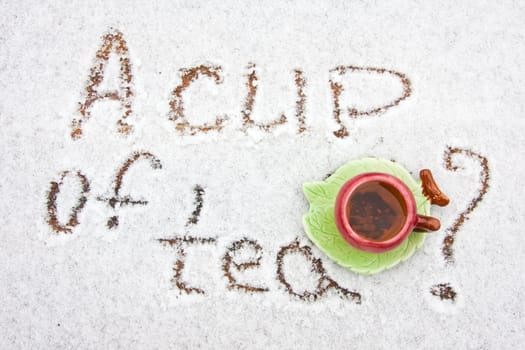 A cup of tea on a snowy background. The inscription on the snow - "a cup of tea?". Saucer shaped leaf. Top view.