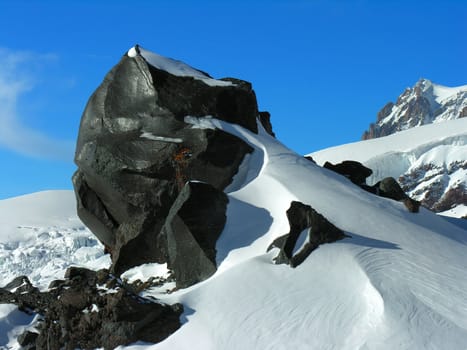 Black rock in a snow on a background of the blue sky.          
