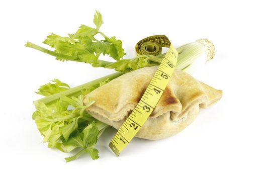 Contradiction between healthy food and junk food using celery and pasty with a tape measure on a reflective white background 