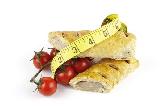 Contradiction between healthy food and junk food using tomatoes and a sausage roll with a tape measure on a reflective white background 