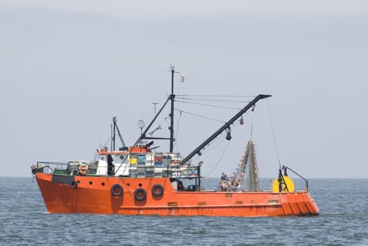 Red fishing boat in the sea, with blue sky.