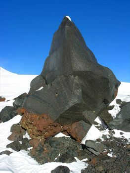 Fragment of a black rock on a snow on a background of the blue sky          