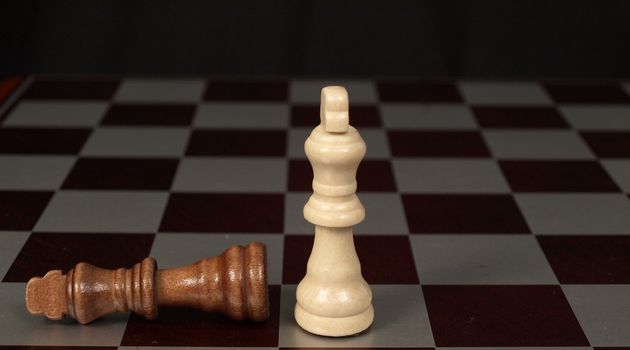 Two kings on a chess board with one knocked over
