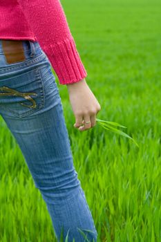 Woman from behind standing in grass, holding it. Copy space on right. Vertical.