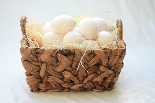 Wicker basket with hay and white eggs