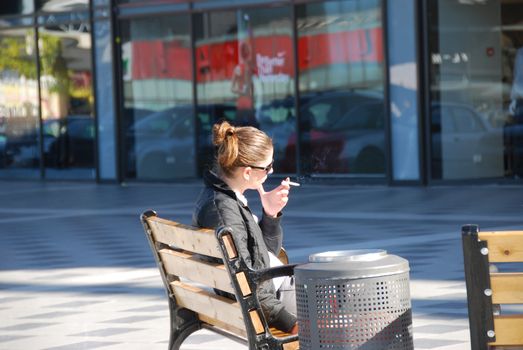 The young smoking woman on a bench