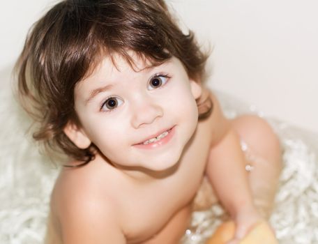 smiling pretty little girl sitting in the bath and ready to wash. Looking directly on photograph