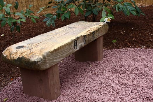 Wooden bench in a garden with Japanese inscriptions.